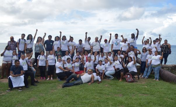 Un grupo de personas está de pie en un prado. Usan las mismas camisetas, estiran los brazos en el aire y sonríen a la cámara. Foto: Alfredo Carías (CRIPDES)